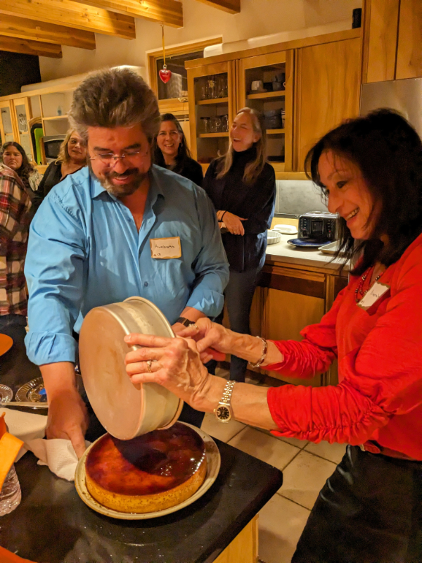 Photo of a man and a woman uncovering a large flan while other people talk and laugh in the background